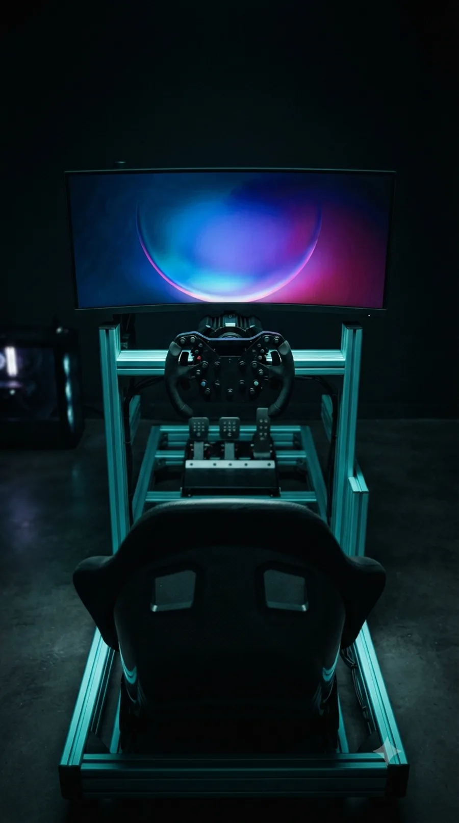 A sim racing rig seen from directly behind: a teal aluminium-profile frame holding a bucket seat, formula-style wheel, three pedals and an ultrawide curved monitor glowing blue and magenta in a dark room.